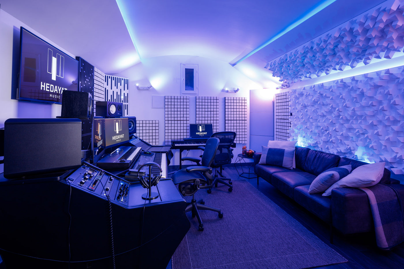 Vue d'ensemble du studio A d'Hedayat Music, régie, canapé et traitement acoustique sous un éclairage violet